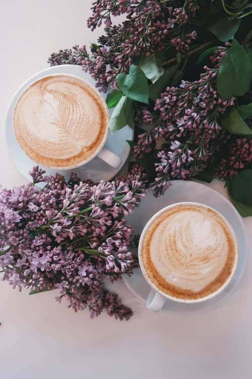 two cups of coffee on a table surrounded by flowers