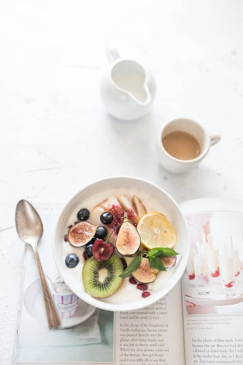 fruit and yoghurt in a bowl alongside a cup of coffee and a magazine