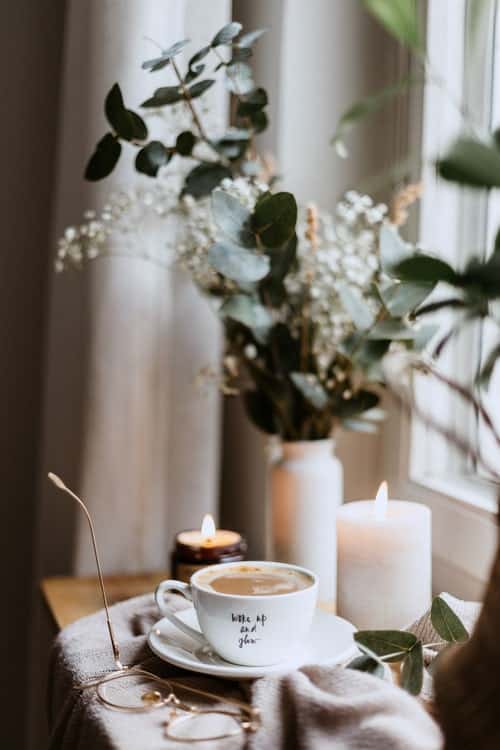 A cup of coffee, glasses, candles and a vase of flowers on a table