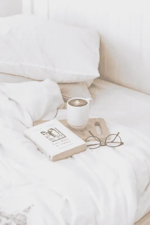 a coffee, book, and glasses on an unmade bed