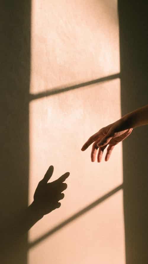 a hand reaching for its shadow on the wall