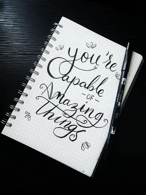a notebook with "you're capable of amazing things" on the front, with a pen on top