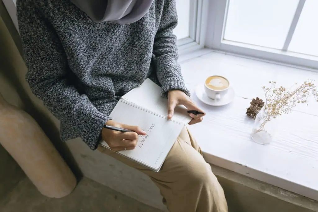 A woman sitting on a window sill with a journal in her lap.