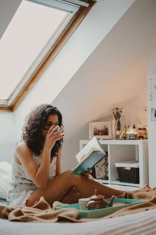 A woman sipping tea and reading a book in bed