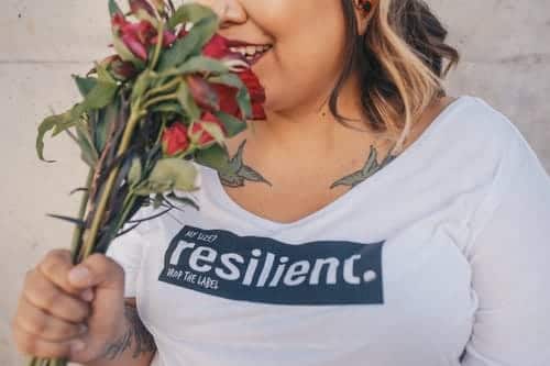 A woman smelling some roses; her t-shirt says "resilient" on it