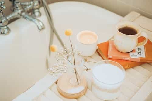 A mug, books, candles and flowers on a bath tray