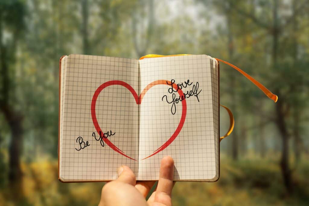 A hand holding up an open notebook with a love heart sketched inside.