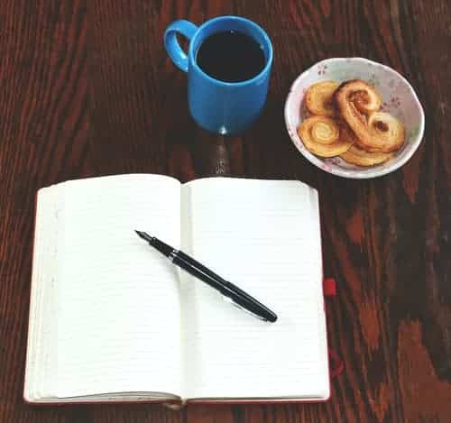 An open journal, biscuits and coffee on a table