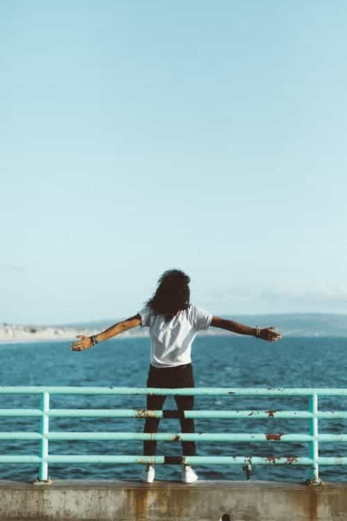 a woman on a pier with her arms outstretched, looking at the sea