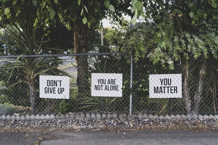 A chain-link fence with signs behind it; the signs read, "don't give up", "you are not alone", and "you matter".