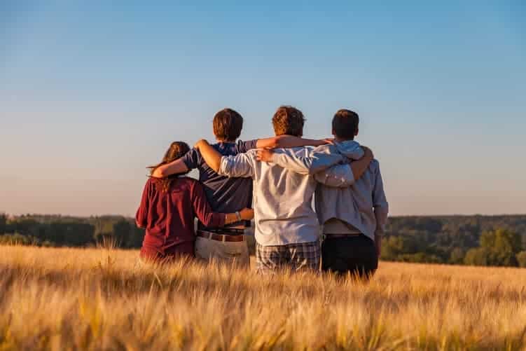 Four people standing in a line in a field with their arms round each other