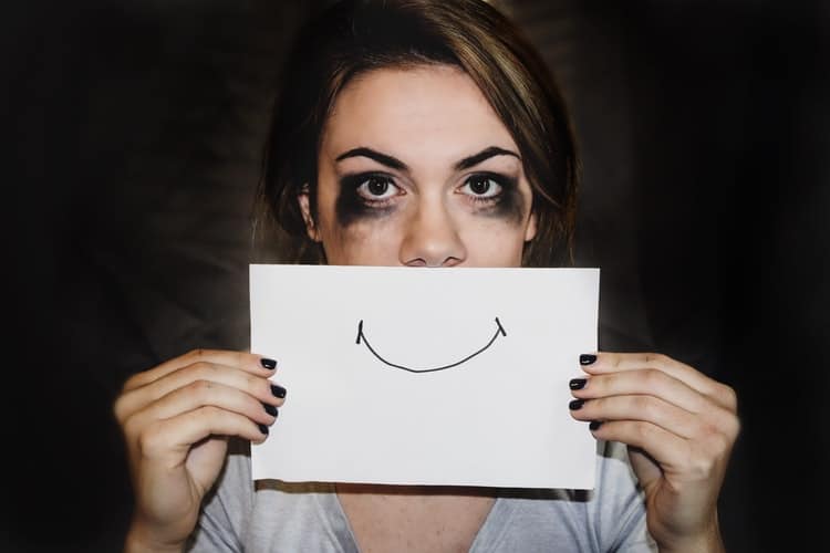 A girl with her eye makeup running, holding a smile drawn on paper in front of her mouth