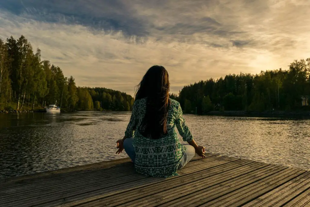 A woman meditating on a dock overlooking a lake